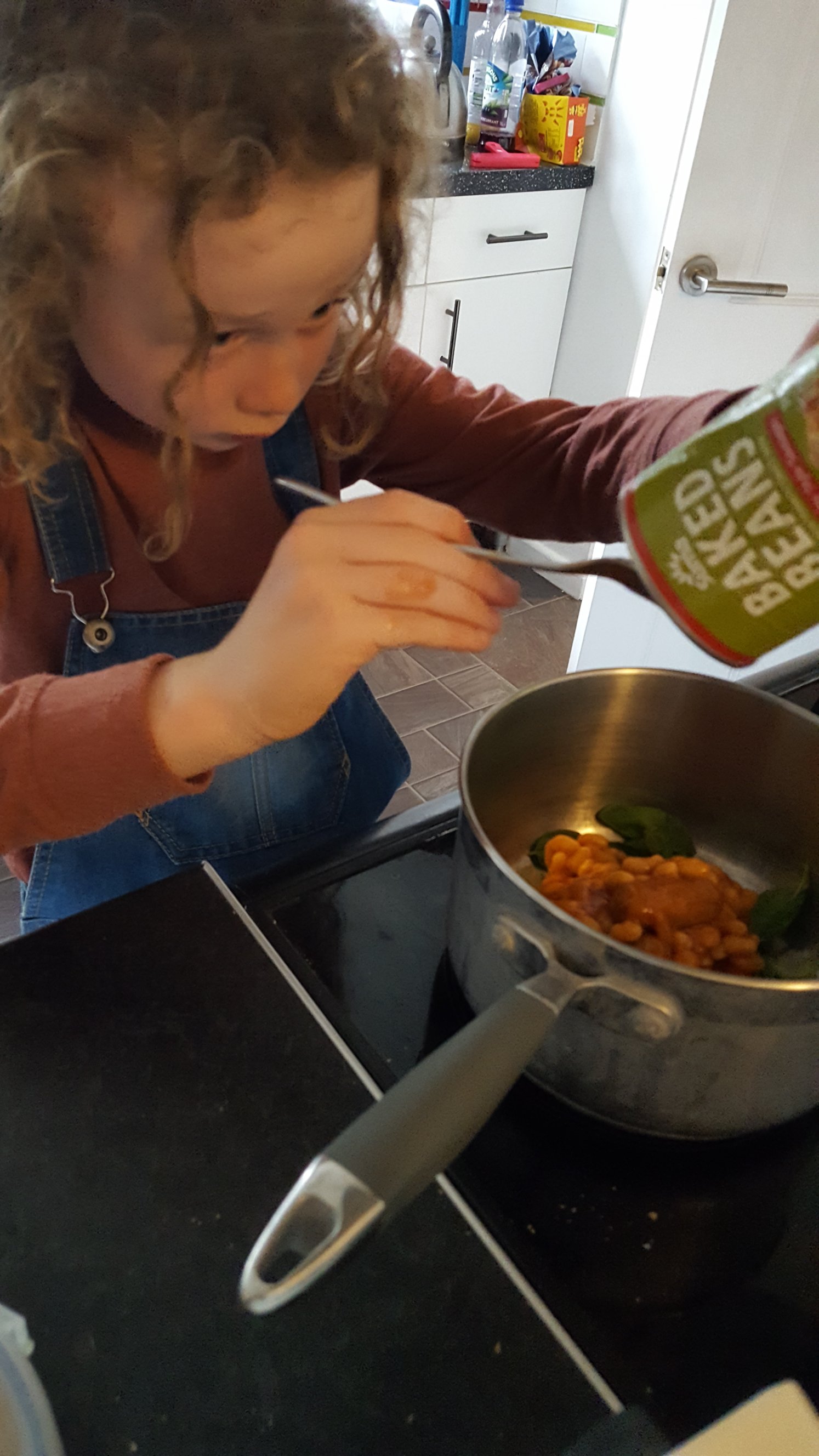 Emptying a tin of beans and sausage into a pan with a spoon